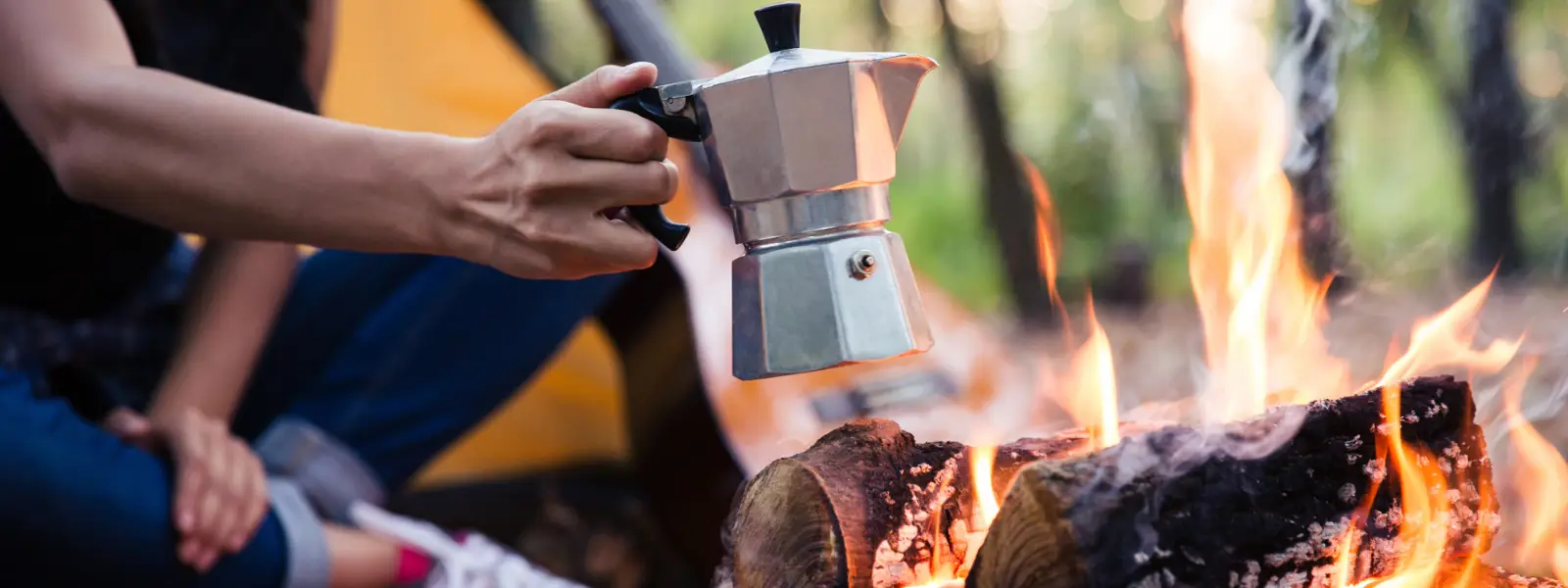 Kvinna som värmer kaffe över öppen eld i skogen